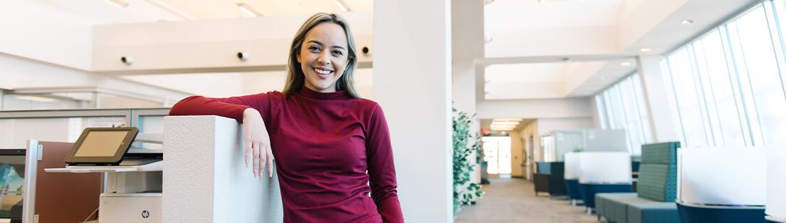 A student stands smiling leaning against a study cubicle in Pima's Desert Vista Campus Library